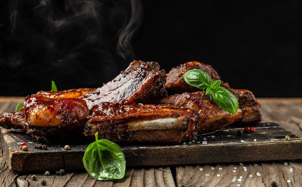 Glazed smoked ribs with fresh basil on a wooden board